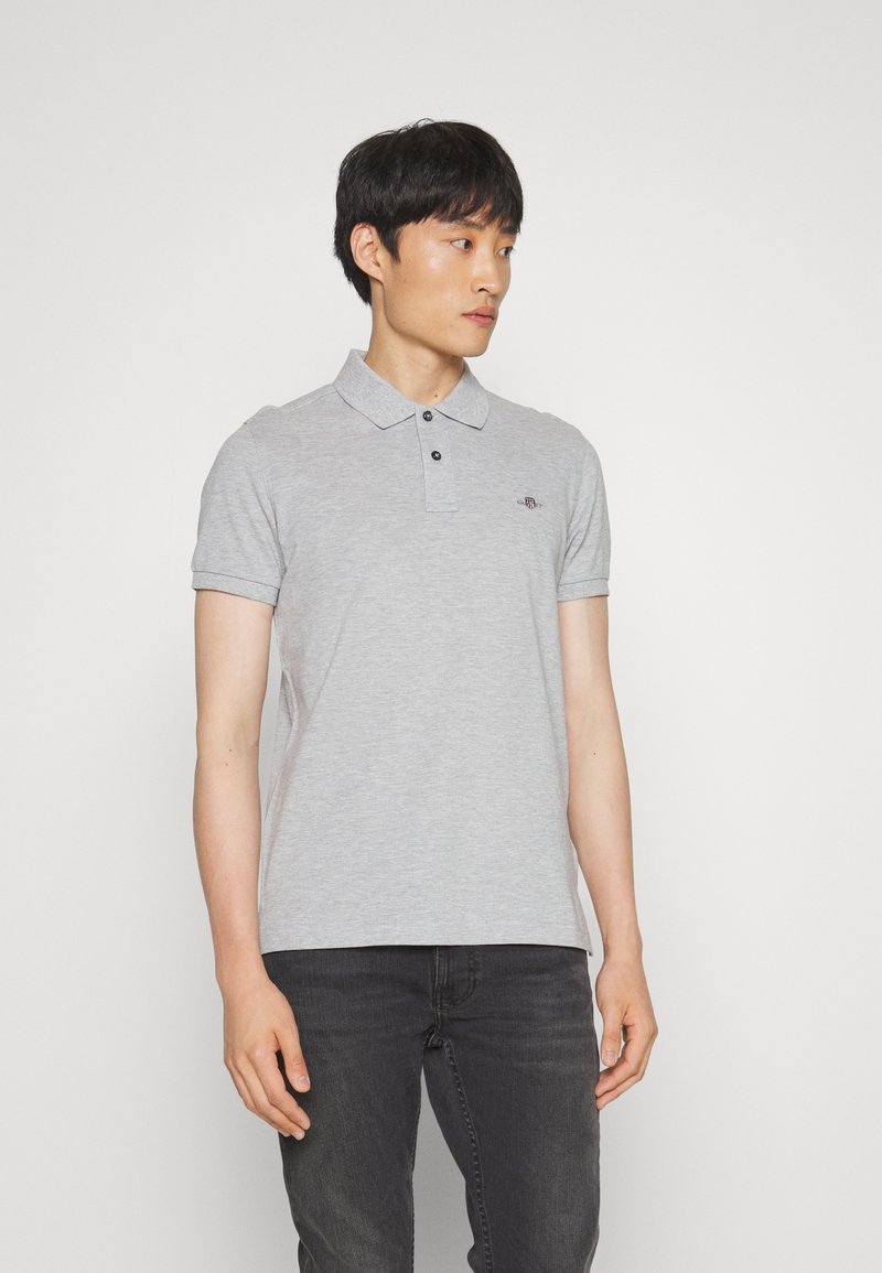 Polo gris de mezcla de algodón, con mangas cortas, un collar y tres botones negros; presenta un pequeño logo en el pecho izquierdo.