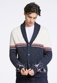 Marinblå och krämfärgad kofta med sjalkrage, knappframsida och festligt mönstrad ok. Har snöflinge-motiv och ribbade muddland.