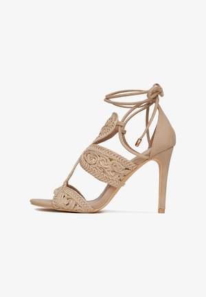 Sandalia de tacón alto beige hecha de material liso con detalles bordados intrincados, diseño de punta abierta y lazos en el tobillo.