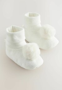 Bottillons en tricot blancs avec un revers replié et deux pompons duveteux à l'avant. Texture douce et design confortable, idéal pour une utilisation intérieure.