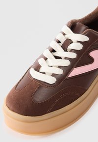 Baskets brunes en cuir lisse et en daim. Lacets crème, accent rose minimal, bout arrondi et semelle plateforme beige.