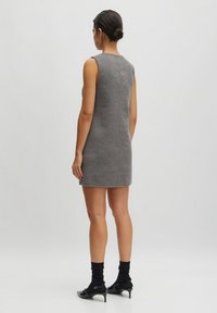 Grijze mouwloze jurk met een strakke pasvorm, rechte zoom, gestructureerde stof en minimale stikdetails. Gedirigeerd met zwarte sokken en schoenen.