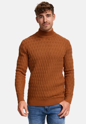 Brun teksturert genser med høy krage og ribbede mansjetter, med et bølgemønster. Bæres sammen med blå denimjeans.