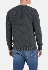 Maglione grigio a maglia con texture a coste, maniche lunghe e scollatura a girocollo. Abbinato a jeans blu con cuciture decorative sui taschini posteriori.
