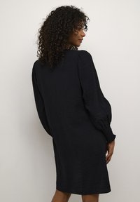 Robe noire texturée avec de longues manches bouffantes et une coupe décontractée. Présente un design simple et un ourlet arrondi. Tissu doux et léger.