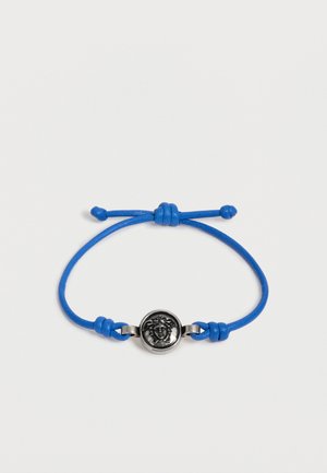 Bracelet cordon bleu réglable avec un emblème tête de Méduse en argent au centre sur fond blanc.