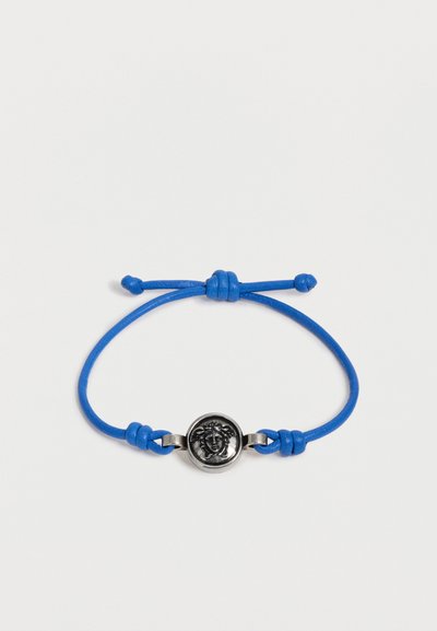 Bracelet cordon bleu réglable avec un emblème tête de Méduse en argent au centre sur fond blanc.