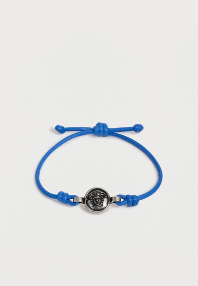 Bracelet cordon bleu réglable avec un emblème tête de Méduse en argent au centre sur fond blanc.