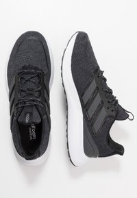 Černé sportovní boty s texturovaným svrškem, které mají tři tmavé pruhy, černé tkaničky a bílou polstrovanou podrážku.