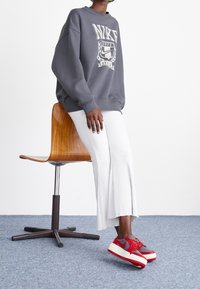 Grå Nike sweatshirt med vit logotyp, i kombination med vita ribbade byxor och röda/grå Nike sneakers. Sömnadsdetaljer och avslappnad passform.