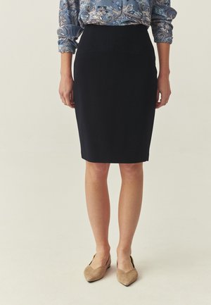 Marineblauer Bleistiftrock mit glatter Textur und taillierter Silhouette. Gestylt mit einer gemusterten blauen Bluse und beigen Schuhen.