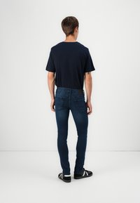 Granatowa koszulka z krótkim rękawem, w zestawieniu z ciemnoniebieskimi dżinsami slim-fit z tylnymi kieszeniami. Uzupełniona czarnymi sneakersami i białymi skarpetkami.