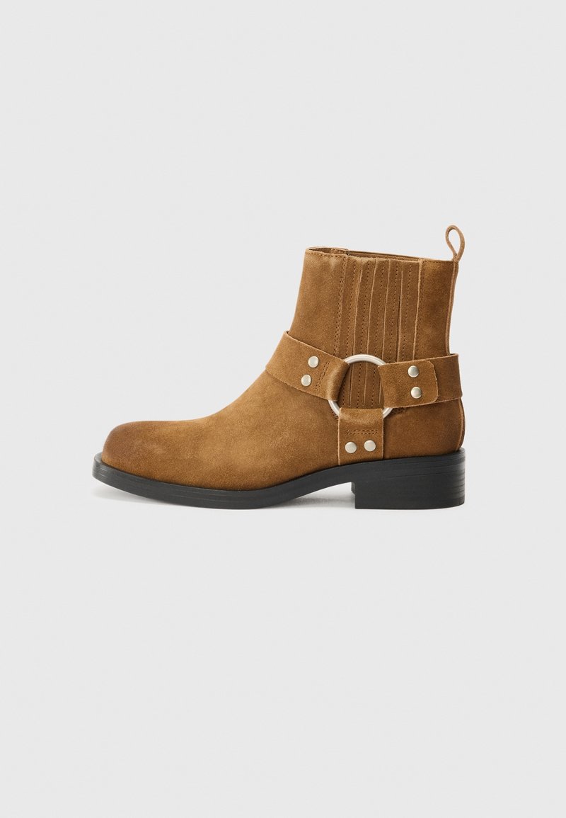 Brązowy zamszowy botek za kostkę z okrągłym noskiem, boczną klamrą i czarną gumową podeszwą. Posiada pionowe przeszycia na cholewce.