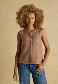 Brązowa wełniana kamizelka z okrągłym dekoltem i siedmioma złotymi guzikami z przodu, połączona z niebieskimi dżinsami. Teksturowana tkanina, bezrękawnik.