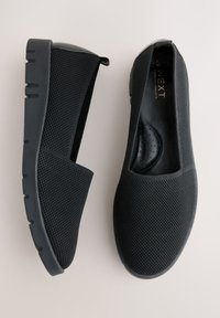 Paire de chaussures noires slip-on en mesh avec semelles épaisses, une chaussure vue de côté et l'autre de dessus montrant une semelle intérieure rembourrée.