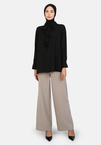 Black long-sleeve blouse with front ruffle detail, paired with beige wide-leg trousers and black pointed-toe heels. Smooth fabric texture.