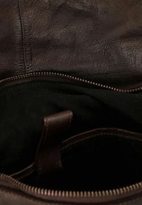 Interno di una borsa in pelle marrone con foderatura in tessuto scuro, dotata di una cerniera e dettagli in pelle a tracolla. Superficie texturizzata visibile.