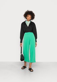 Camisola cropped preta de mangas longas, calças verdes de perna larga, bolsa preta e sandálias pretas. Textura suave com um corte descontraído e cintura elástica.