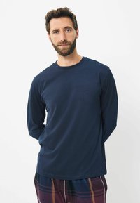 Marineblaue Langarmbluse aus weichem Stoff, mit klassischem Rundhalsausschnitt und lockerer Passform. Sichtbare Nähte entlang der Schulternähte.