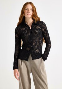 Svart spets skjorta med knappar, blommönster, långa ärmar och krage. Kombinerad med ljusbeige skräddarsydda byxor.