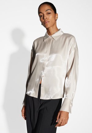 Light beige satin shirt with a collar and button closure, featuring long sleeves and a smooth, shiny texture. Worn with black pants.