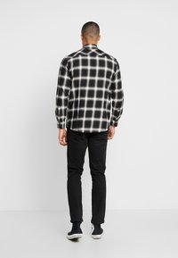 Black and white plaid long-sleeve shirt with a button-down collar, lightweight fabric, and a straight fit, paired with black pants and sneakers.