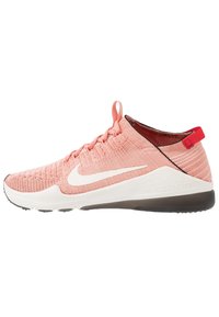 Ljust rosa träningssko med en vit Nike-swoosh, nära vy som framhäver den texturerade överdelen och den kontrasterande mörka sulan.