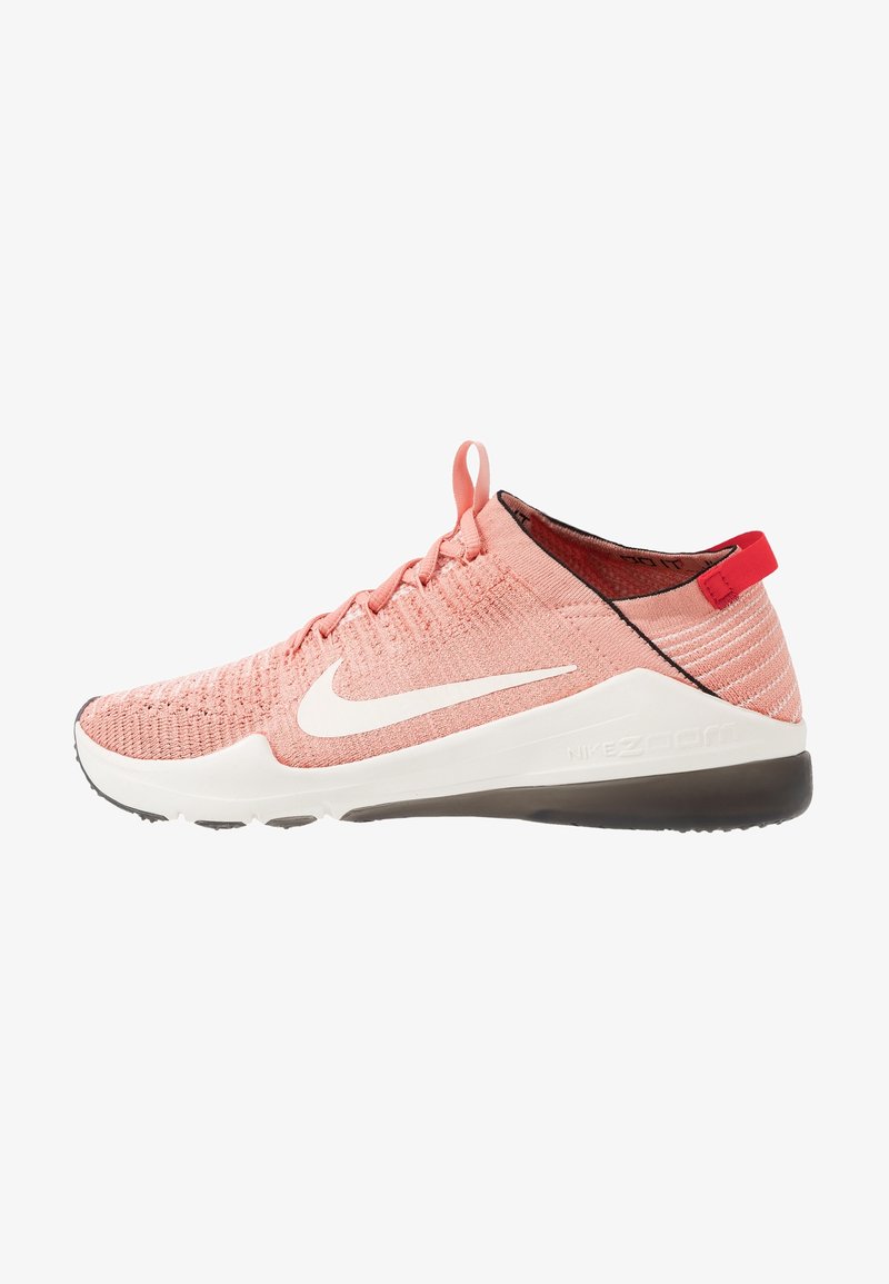Ljust rosa träningssko med en vit Nike-swoosh, nära vy som framhäver den texturerade överdelen och den kontrasterande mörka sulan.