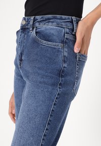 Μπλε τζιν παντελόνι με εφαρμοστή σχεδίαση, διαθέτει ψηλή μέση, πέντε τσέπες και ελαφριά φθορά στους μηρούς. Υλικό από βαμβακερό μίγμα.