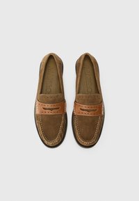Brown suede loafers with a contrasting tan leather band, decorative perforations, white stitching, and a flexible black sole.