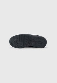 Μαύρη σόλα αθλητικού παπουτσιού με υφασμένο καουτσούκ, με σχέδια για πρόσφυση και καθορισμένα αυλάκια. Περιλαμβάνει λεπτομέρεια λογότυπου κοντά στη φτέρνα.