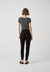 Schwarz-weiß gestreiftes Kurzarmoberteil mit rundem Halsausschnitt, kombiniert mit schmalen schwarzen Hosen und flachen Sandalen, von hinten betrachtet.