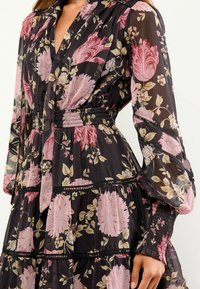 Rochie neagră cu flori, confecționată din material transparent, având mari trandafiri roz, design în straturi, talie elasticizată și mâneci lungi, bufante.