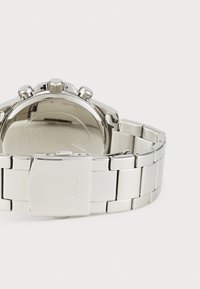 Montre chronographe en métal argenté avec un bracelet en acier inoxydable poli, des sous-cadrans et un fermoir à rabat. Le dos présente des détails gravés.