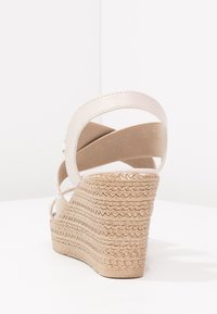 Sandale compensée avec talon en jute tissé texturé, brides en tissu beige et un accent lisse et brillant le long du talon.