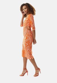 Orange, fitted dress with wavy white pattern, three-quarter sleeves, and side cutout, paired with strappy red high-heeled sandals.