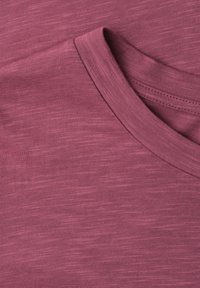 Gros plan d'un t-shirt violet délavé à col rond montrant la fine texture du tissu et les coutures détaillées autour du col.