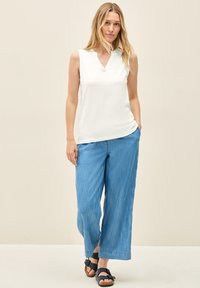 Weißes ärmelloses Oberteil mit einem eingeschnittenen Kragen, kombiniert mit hellblauen weitem Hosen und marineblauen Sandalen. Glattes Material mit lockerer Passform.