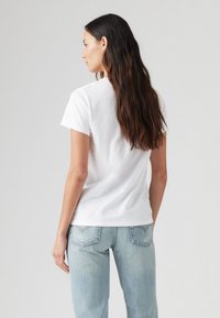 T-shirt en coton blanc à manches courtes, avec un col rond et une texture lisse. Porté avec un jean en denim bleu clair. Vue de dos centrée sur le t-shirt.