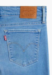 Svetle modré džíny z denimu s hnědou koženou nášivkou na pase. Obsahují charakteristický design zadní kapsy a kontrastní žluté stehy.