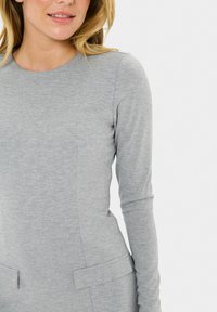 Gray long-sleeve dress in soft, textured fabric with a round neckline and two front pockets. Minimalist design with tailored fit.