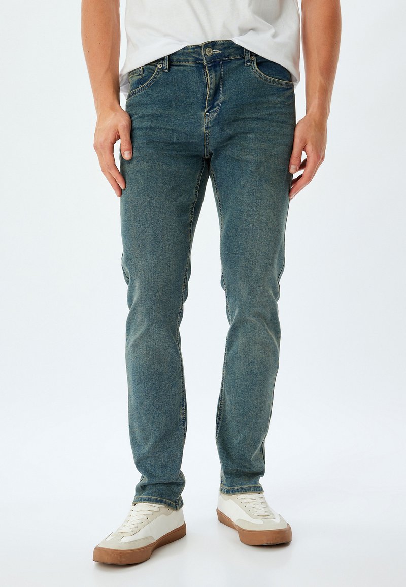 Jeans in denim blu con una vestibilità slim, dotati di chiusura con zip, cinque tasche e un leggero effetto sbiadito. Abbinati a sneakers off-white.