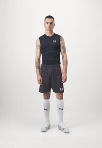 Fekete ujjatlan sportfelső, sötétszürke sort narancssárga részletekkel, fehér térdzokni logóval, világoskék focicipő, és tetoválások.