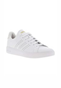 Zapatillas blancas con parte superior de piel suave, diseño perforado en el lateral y suela de goma. Presenta un logo dorado sutil en la lengüeta.