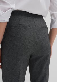 Pantalons tailleur gris en tissu texturé. Comprend deux poches arrière et une taille haute. Le design présente une silhouette élégante et ajustée.