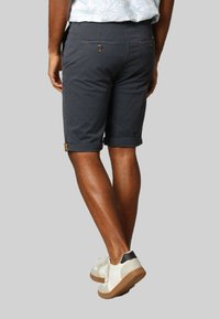 Marineblauwe katoenen shorts met opgerolde boorden, twee achterzakken met knoopsluitingen en een slim fit, gecombineerd met witte sneakers.
