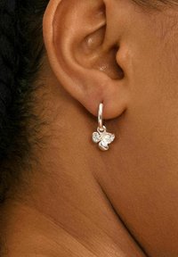 Boucle d'oreille en argent avec un design floral, présentant une finition polie et de petits accents détaillés, affichée sur un fond de teinte de peau.
