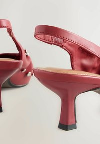 Punaiset nahkakengät korkealla korolla, joissa on malli slingback, neliömäiset korot ja koristeelliset hopeiset yksityiskohdat. Sujuva pinta ja kiiltävä viimeistely.