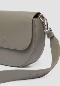 Hellgraue Leder-Crossbody-Tasche mit runder Form, magnetischem Klappenverschluss und strukturiertem Finish. Ausgestattet mit einem abnehmbaren Schultergurt mit prägierter Schrift.