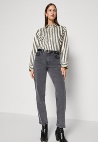 Chemise à rayures crème et noire, associée à un jean taille haute gris et des bottines noires, dotée d'une boucle de ceinture ronde.